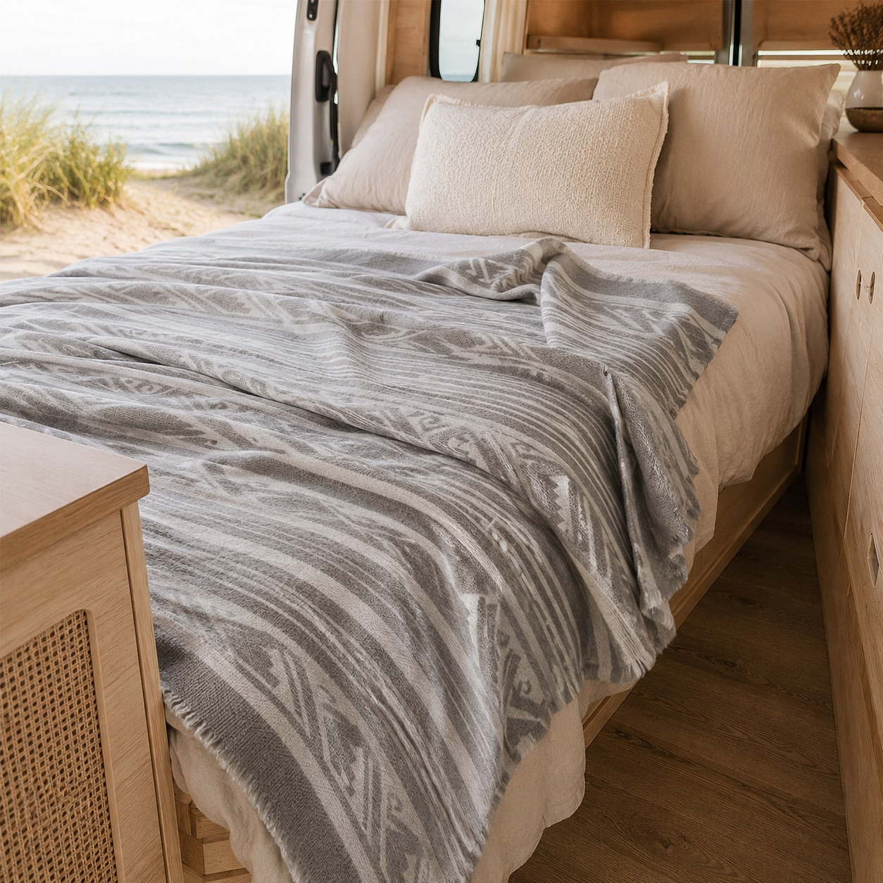 Bed in campervan with patterned llama wool blanket and pillows with beach view