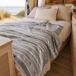 Bed in campervan with patterned llama wool blanket and pillows with beach view
