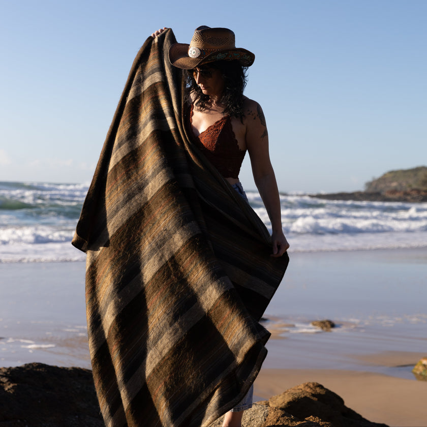 Woman holding  up  alpaca blanket at the beach with waves in the background