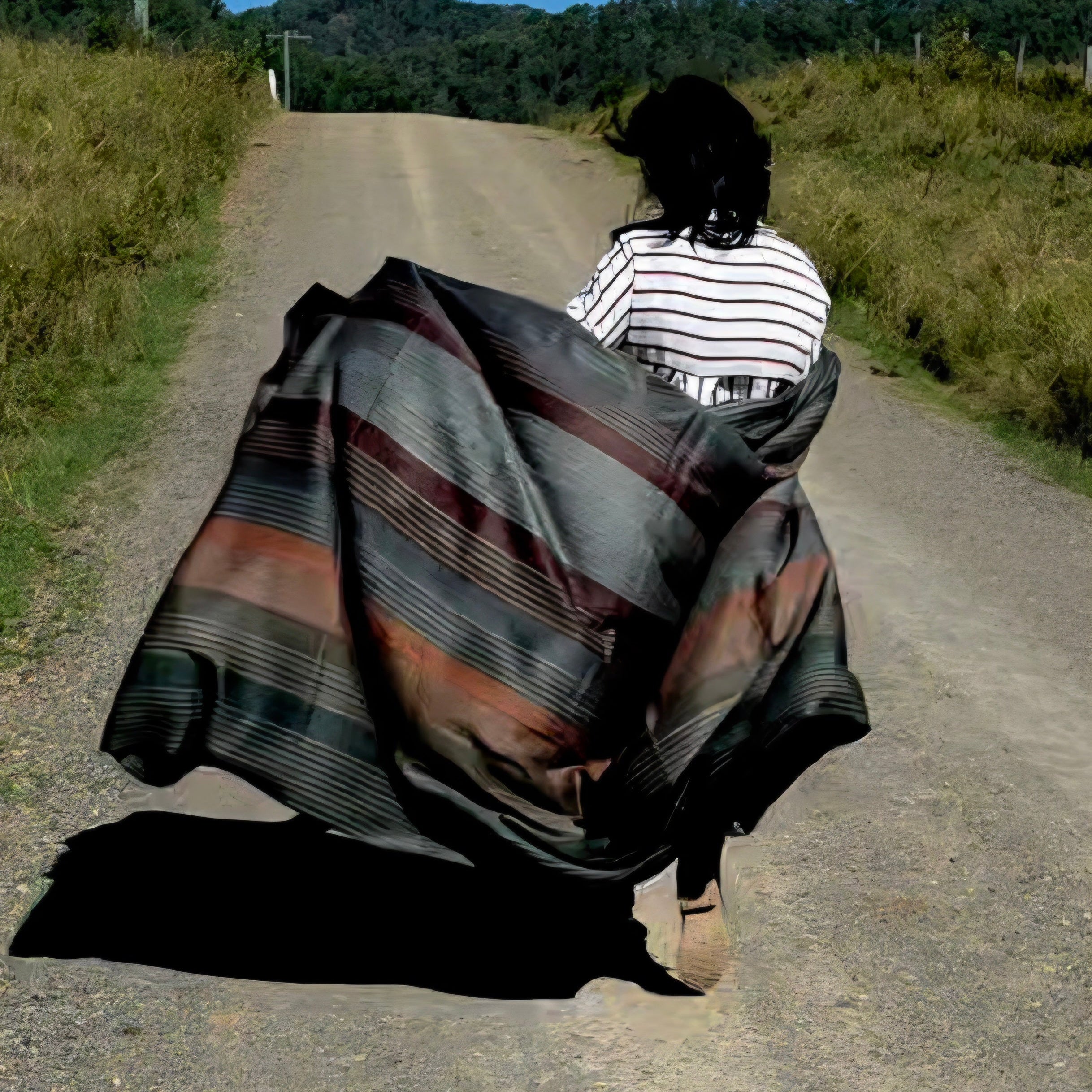 Person walking on a dirt road with a large alpaca wool blanket draped over them