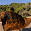 Person wearing a patterned llama wool blanket on an Australian beach with greenery in the background