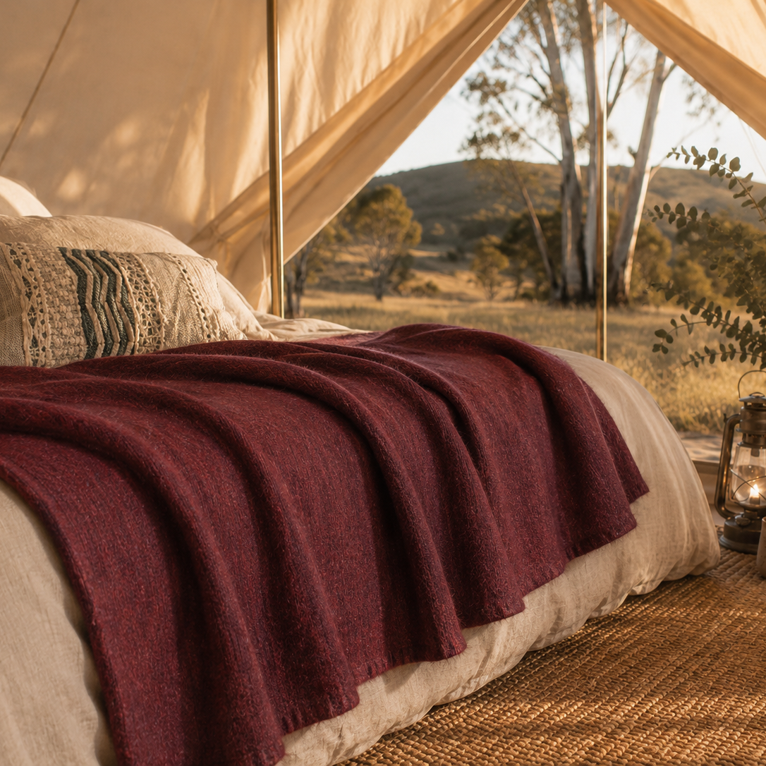 Bed with burgundy baby alpaca wool blanket inside a tent with scenic Australian outdoor view